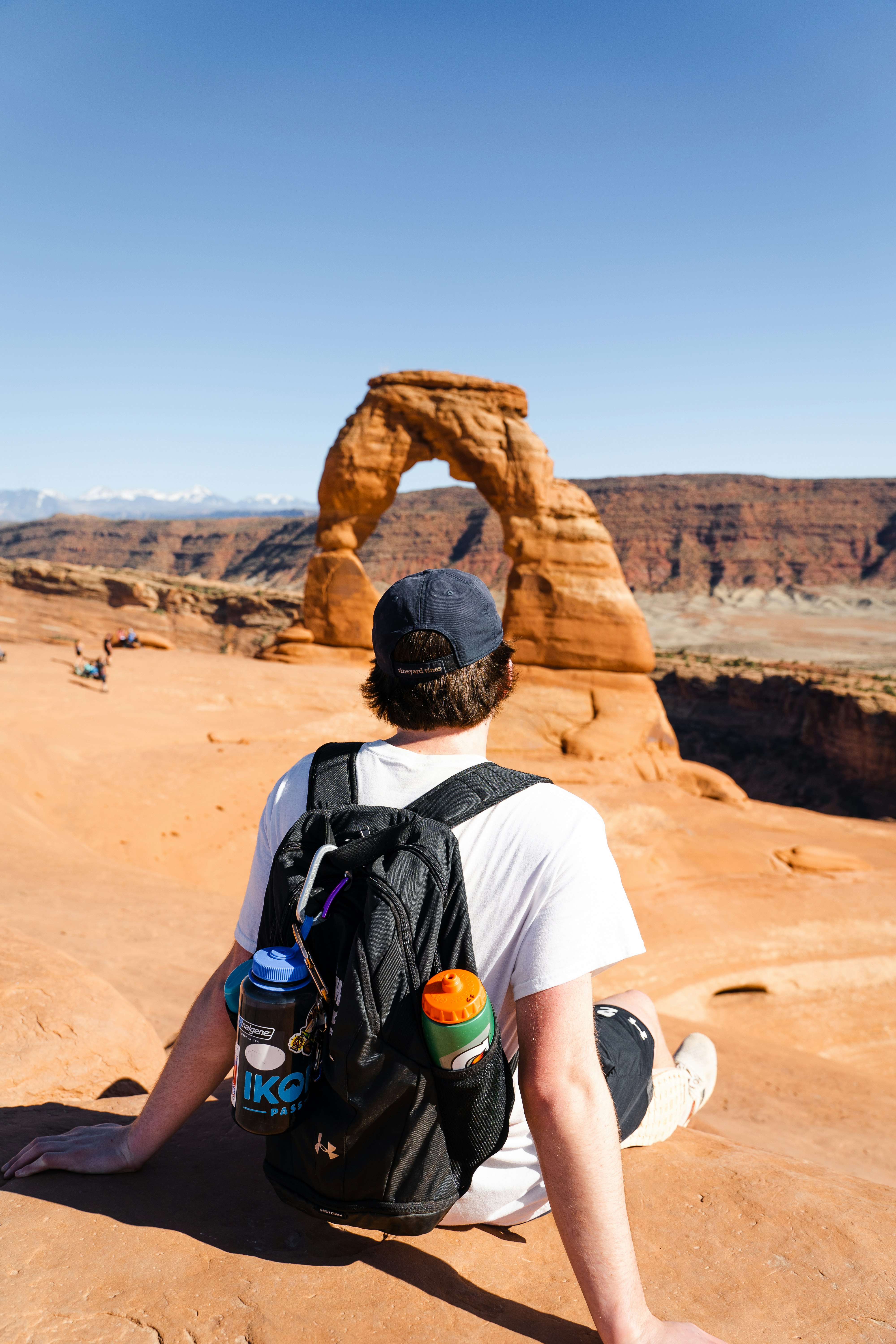 man in white t-shirt wearing black backpack standing on brown rock formation during daytime